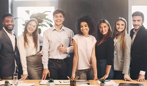 A diverse group of young professionals, including men and women, standing together in an office setting